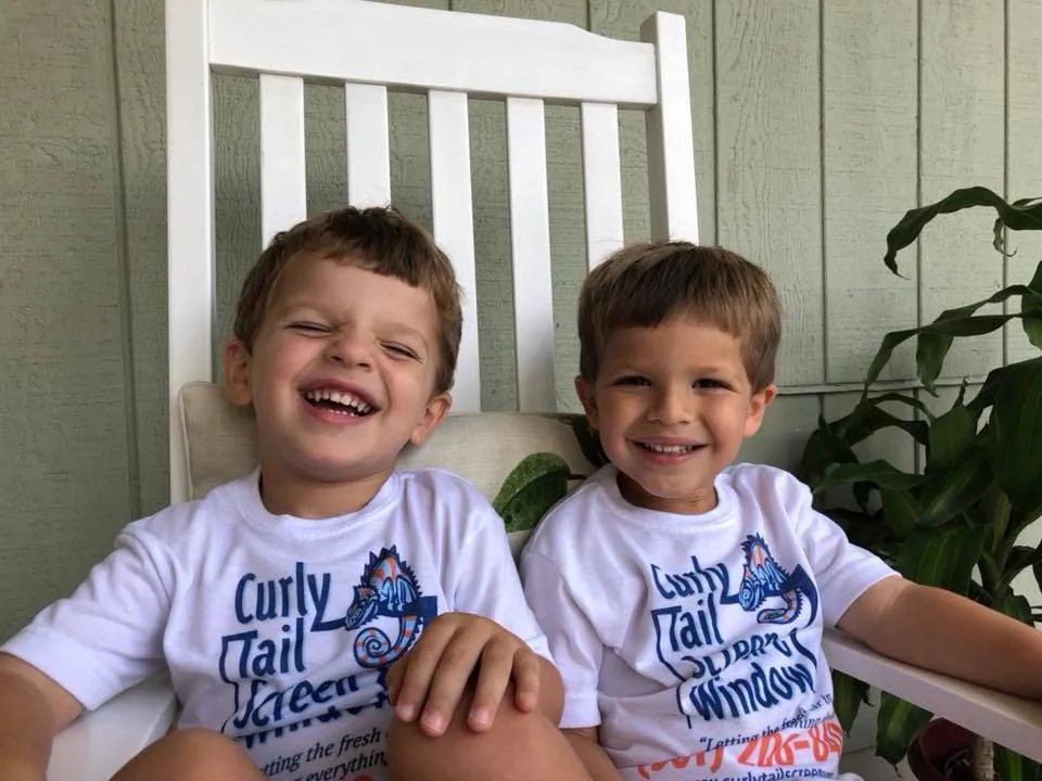 Twin boys wearing Curly Tail Screen & Window t-shirts, smiling on a porch